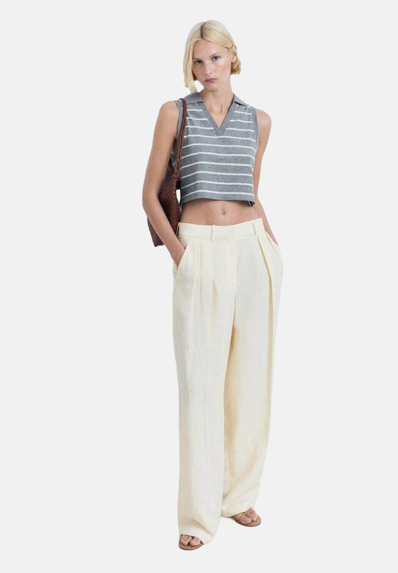 Pruhovaný šedobiely bezrukávový crop top s výstrihom do V, kombinovaný s vysokými, širokými nohavicami v krémovej farbe.