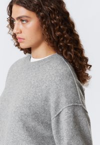 Pull en polaire gris avec un col rond et des épaules tombantes, offrant une texture douce et un design minimaliste.