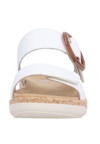 White sandals with two adjustable straps, featuring a round brown buckle, soft insole, and a textured light tan outsole.