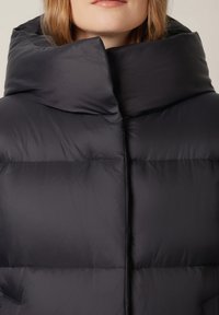Czarna kurtka puchowa z wysokim kołnierzem, z pikowanym wzorem i gładką teksturą. Brak widocznych zapięć lub elementów metalowych.