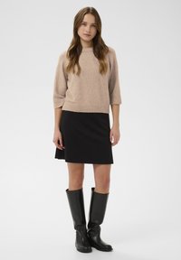 Bézs kötött rövid ujjú pulóver bordázott szegéllyel, hozzá illeszkedő fekete szoknya és térdig érő fekete bőr csizma.