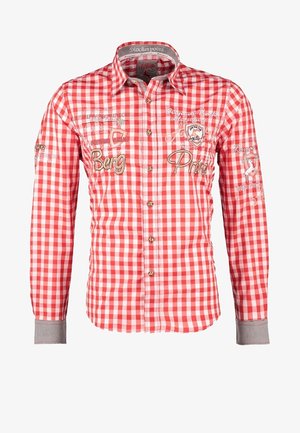 Homme portant un lederhose traditionnel en cuir marron avec bretelles, chemise rouge et blanche à carreaux, chaussettes grises et chaussures marron.