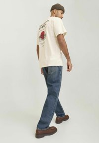 Cream t-shirt with graphic print on the back, paired with blue jeans and brown boots. Casual fit with short sleeves and a round neckline.