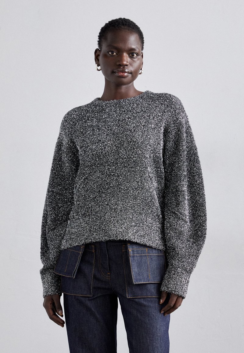 Grå og sort meleret strikket sweater med rund hals og lange, voluminøse ærmer, parret med mørke denim jeans med dobbelte baglommer.