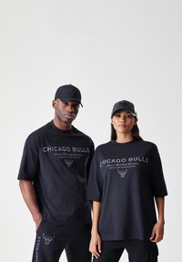 Černá módní souprava obsahující oversized trička s nápisem "CHICAGO BULLS" a logem býka, doplněná o odpovídající kšilty a kalhoty.