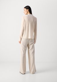 Lys beige langermet topp med en subtil krage, kombinert med vide rillede bukser i en matchende nyanse, som skaper et koselig, teksturert utseende.