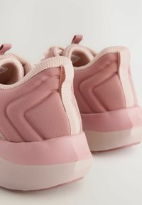 Chaussures de sport roses avec un tissu texturé, des semelles en caoutchouc lisses et des accents imprimés. Comprend des tirettes pour faciliter l'enfilage.