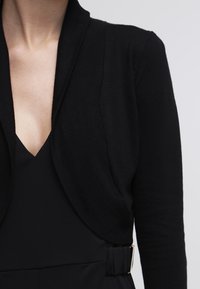 Schwarze Strickjacke mit offenem Design, geripptem Textur und langen Ärmeln. Verfügt über eine taillierte Silhouette und einen tiefen V-Ausschnitt.