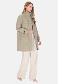 Világos bézs színű ballonkabát négy elülső zsebbel, magas gallérral és hosszú ujjal, krémszínű, bőszárú nadrággal rétegezve.