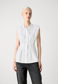 Bluză albă fără mâneci, cu un corset ajustat, guler și detalii subtile de pliere. Fabricată dintr-un material neted, se potrivește cu pantaloni negri cu talie înaltă.