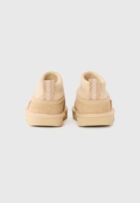 Bottines beige avec un dessus en daim texturé, un col élastique et un détail tissé contrastant à l'arrière, dotées d'une semelle en caoutchouc.