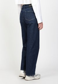 Dunkelblaue Denim-Jeans mit geradem Bein, aufgesetzten Gesäßtaschen und einem gepunkteten Bund, kombiniert mit weißen Sneakern.