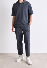 Koszulka polo z krótkim rękawem w kolorze granatowym z kołnierzykiem, połączona z dopasowanymi granatowymi spodniami. Białe sneakersy z teksturowaną podeszwą dopełniają całość.