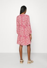 Abito con stampa floreale in rosso e bianco, maniche lunghe, vestibilità rilassata, vita arricciata e orlo con volant. Design semplice e tessuto leggero.