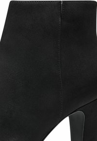 Gros plan sur une bottine en daim noir avec un talon bloc haut et des coutures visibles le long du côté.