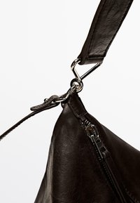 Borsa a mano in pelle nera con una superficie texture, dotata di una chiusura in metallo argentato e una cerniera. La tracolla è anch'essa in pelle, a dimostrazione della sua resistenza.