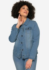 Veste en denim bleu clair avec un col, des boutons sur le devant, deux poches poitrine et des manches longues, offrant une coupe classique et un léger délavage.