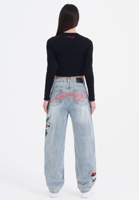 Black cropped long-sleeve shirt with red embroidered text, paired with light blue wide-leg jeans featuring colorful embroidered patches.