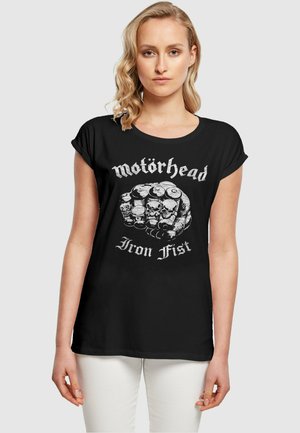 Svart t-skjorte med korte rullede ermer, med et grafisk motiv av en neve pyntet med kranier og teksten "Motörhead Iron Fist" i hvitt.