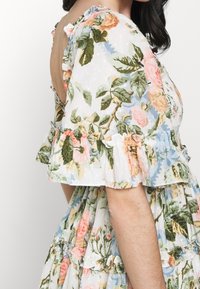 Vestido floral en tejido ligero y texturizado. Fondo blanco roto con patrones florales en rosa, verde y azul. Mangas y dobladillo con volantes.