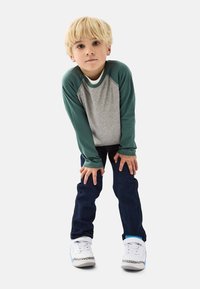 Langærmet grå og grøn raglan skjorte parret med mørke jeans og hvide sneakers. Skjorten har kontrastfarvede ærmer; afslappet pasform.