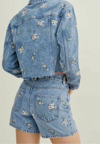 Conjunto de chaqueta de mezclilla y pantalones cortos con bordado floral en azul. Presenta mangas cortas y dobladillo deshilachado en la chaqueta; bolsillos traseros en los pantalones cortos.