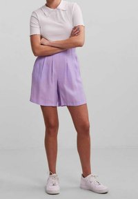 Ljuslila veckade shorts som bärs med en vit kortärmad pikétröja, tillsammans med vita sneakers. Slät tygtextur, avslappnad design.