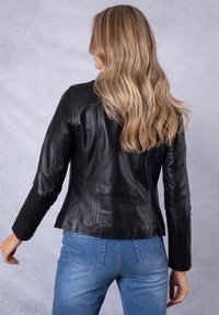 Black leather jacket with a fitted design, smooth texture, and visible seam details. Pairing with light blue denim jeans.