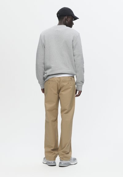 Felpa grigia, pantaloni beige larghi e sneakers grigie. Design semplice, texture morbida, vestibilità casual. Vista da dietro su uno sfondo bianco.