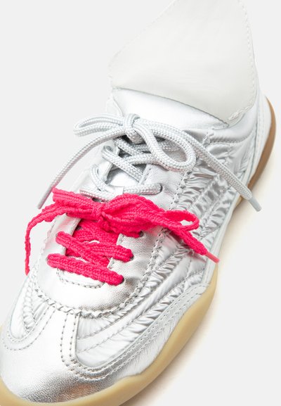 Baskets argentées avec double lacets, gris sur le dessus et rose vif noué en nœud, avec des coutures texturées et une semelle couleur cuir clair.