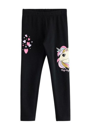 Ung pige med krøllet hår iført en lilla bluse med lange ærmer og sorte leggings, begge med farverige enhjørninge motiver.