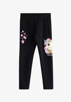 Ung pige med krøllet hår iført en lilla bluse med lange ærmer og sorte leggings, begge med farverige enhjørninge motiver.