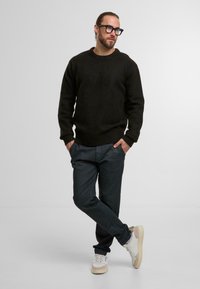 Dunkelgrauer Strickpullover mit Rundhalsausschnitt, kombiniert mit schiefergrauen, schmal geschnittenen Hosen. Weiße Sneakers mit beigen Akzenten. Minimalistisches Design.