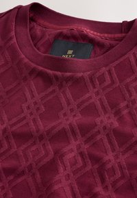 Burgundy sweatshirt featuring a textured geometric pattern, round neckline, and tag with "NEXT" branding inside.