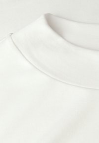 Camiseta de algodón blanca con un cuello redondo acanalado. La tela tiene una textura suave, mostrando costuras finas a lo largo de los bordes.