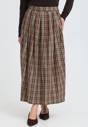 Person wearing a brown plaid pleated midi skirt, dark long-sleeve top, and dark brown flats, with hands in skirt pockets.