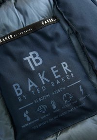 Doublure intérieure d'une veste marine avec une étiquette d'entretien imprimée. Comprend des logos, des symboles pour l'imperméabilité, la durabilité et un "remplissage recyclé".