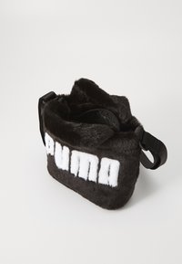 Svart fuskpälsväska med en mjuk textur, med en vit "PUMA"-logotyp. Inkluderar ett överdrag med dragkedja och ett svart justerbart axelband.