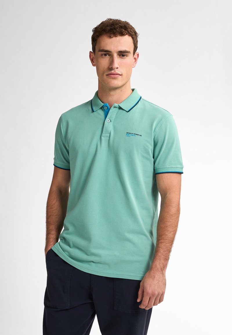 Svetlozelená polo košeľa s golierom, má dvojité gombíkové zapínanie a modré akcenty na golieri a rukávoch. Zobrazuje malý text.