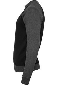 Sweatshirt à manches longues avec corps noir et manches gris foncé, poignets et col côtelés, montré de profil sur fond blanc.