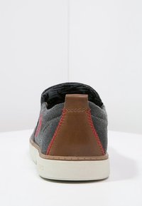 Chaussure en toile grise avec des coutures rouges et des accents en cuir marron. Design à profil bas avec une semelle en caoutchouc et une forme élégante et minimaliste.