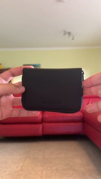 Zwarte leren portemonnee met een gladde textuur, ronde randen en een ritsluiting. Bevat subtiele branding aan de voorkant.