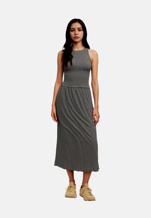 Czarna i biała sukienka maxi bez rękawów z dopasowanym gorsetem i lejącym się dołem, zestawiona z jasnobeżowymi sneakersami.