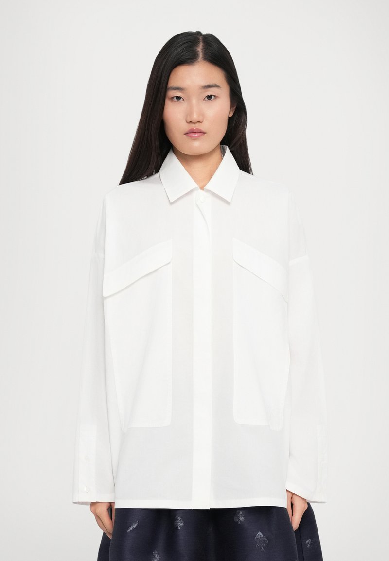 White button-up shirt with a classic collar, long sleeves, two front pockets, and a loose fit. Lightweight fabric with a smooth texture.