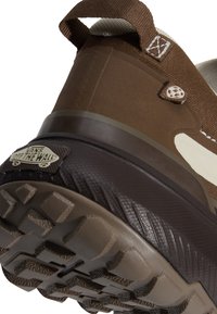 Gros plan sur le talon d'une basket Vans marron montrant la semelle texturée, la languette et le logo "Vans Off The Wall" au dos.