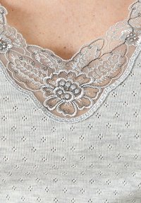 Top de tirantes gris con un escote de encaje y bordado floral, tejido texturizado y un patrón de diamantes en toda la prenda.