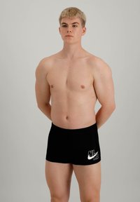 Shorts de bain noirs Nike avec un logo blanc sur le côté gauche, design épuré, texture lisse et coupe ajustée.