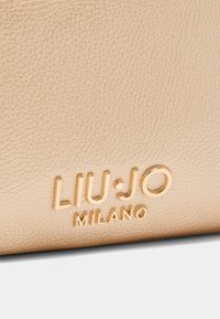 Bežani teksturirani kožni materijal s utisnutim zlatnim logotipom "LIU·JO MILANO" i glatkim akcentima. Prikaz izbliza koji ističe materijal i brend.