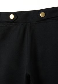 Primer plano de una tela negra que muestra la sección superior con detalle de costura y dos botones a presión dorados en la cinturilla.