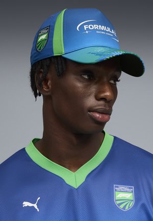 Młody mężczyzna w niebiesko-zielonej czapce Formula 1 Racing League i dopasowanej koszulce z logo Grand Prix São Paulo 2026.